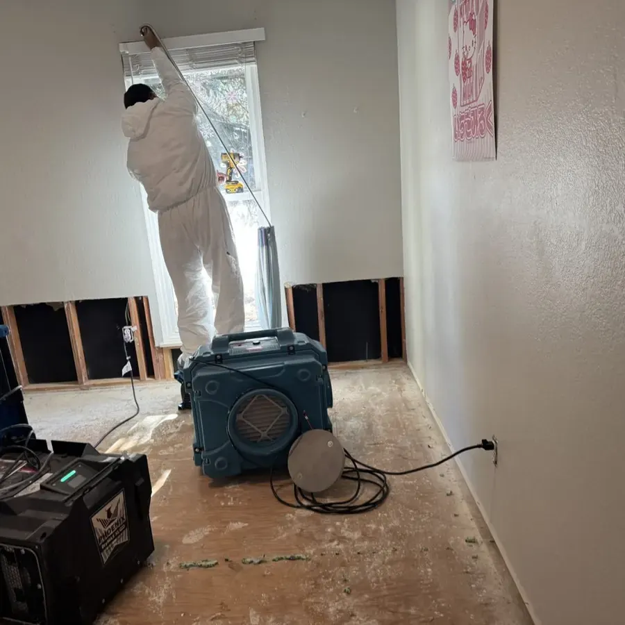 A technician in a protective suit beside flood-cut hallway walls and a dehumidifier inside an Arvada home