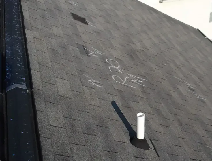Asphalt shingle roof with chalk marks circling hail hits around a vent pipe
